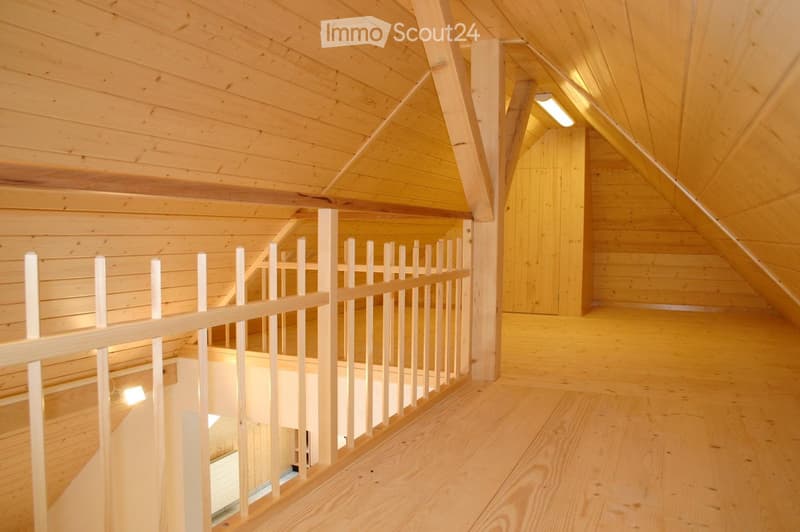 Wooden hallway with slanted ceiling, wooden railing, and warm lighting.