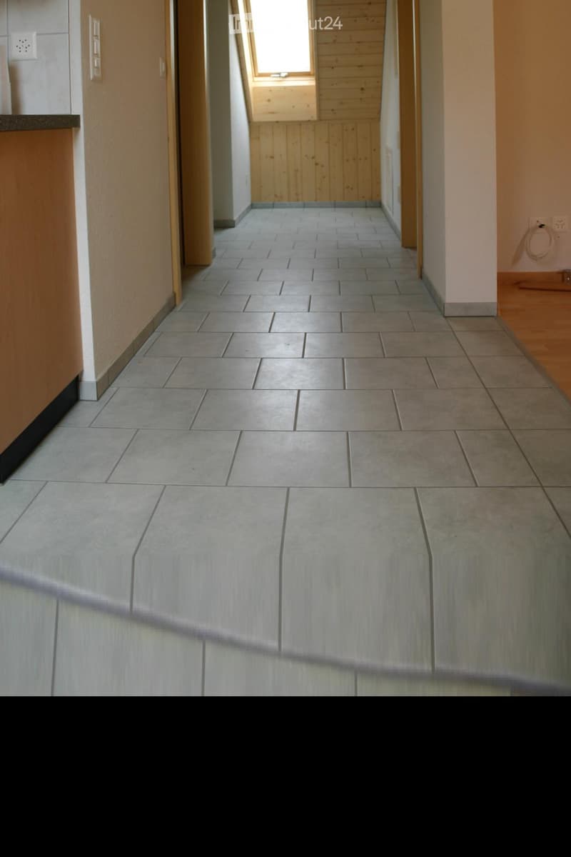 Empty hallway with tiled floor, wooden paneling on one side, and a small skylight window at the end.