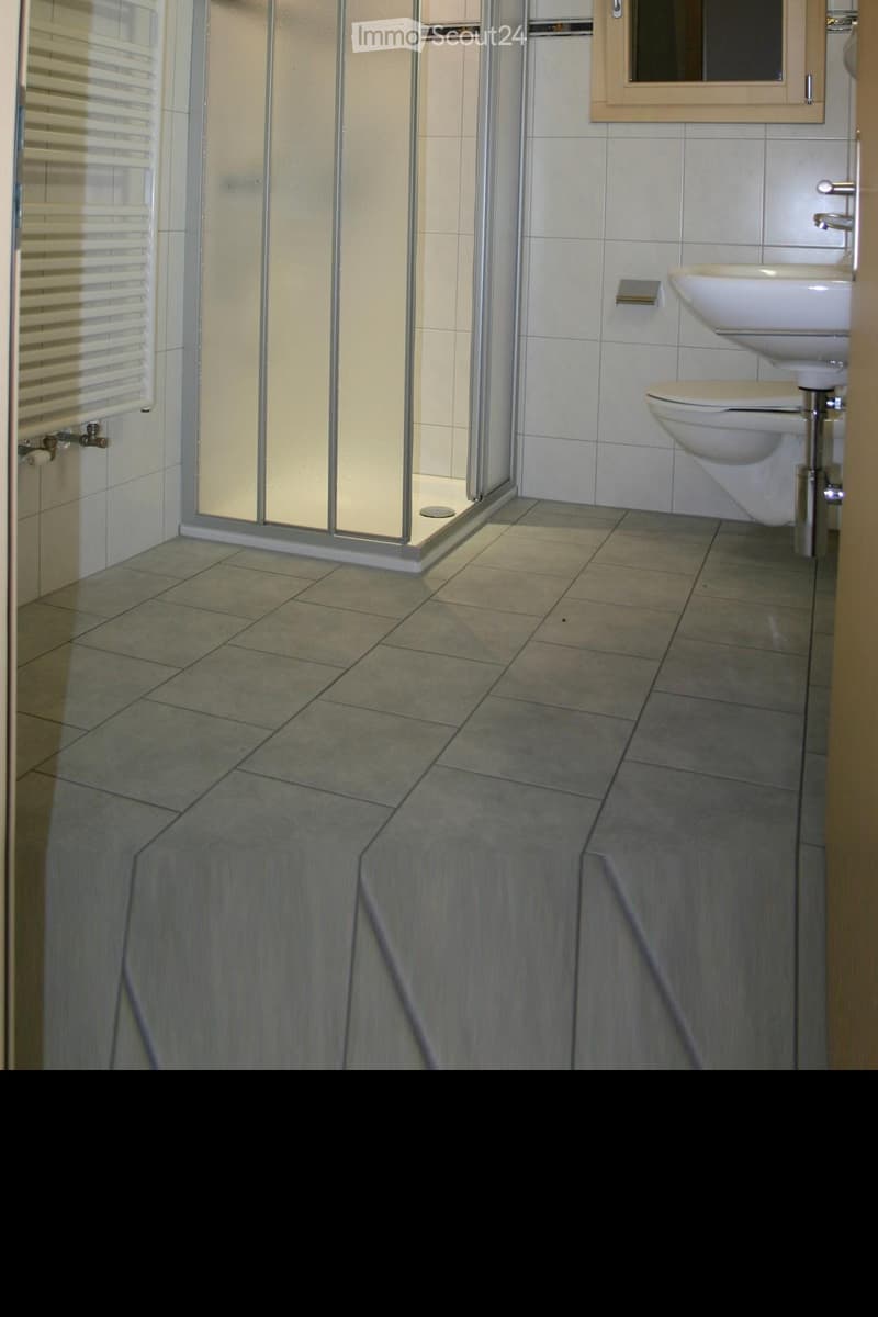 Modern bathroom with tiled walls and floor, featuring a glass-enclosed shower, a toilet, and a sink.