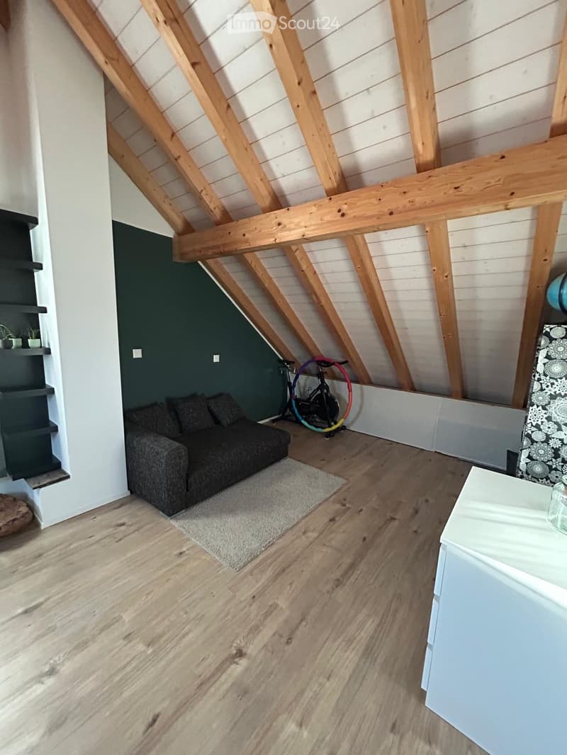 Loft-style room with wooden beams, grey sofa, small rug, bicycle, and built-in shelves.