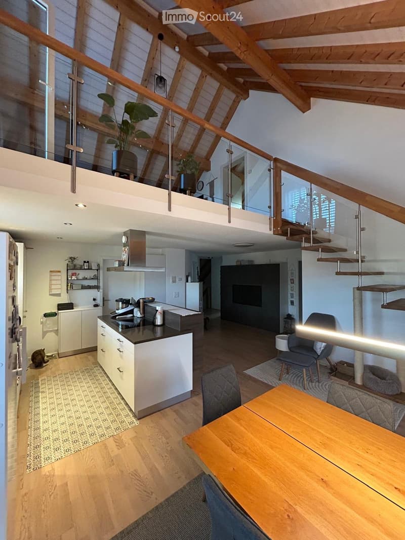 Open-plan living and dining area with a modern kitchen, wooden flooring, and a cat-friendly setup including a cat tree, cat bed, and litter box. The space features a kitchen island, a sofa, a dining table, and a staircase leading to an upper level.