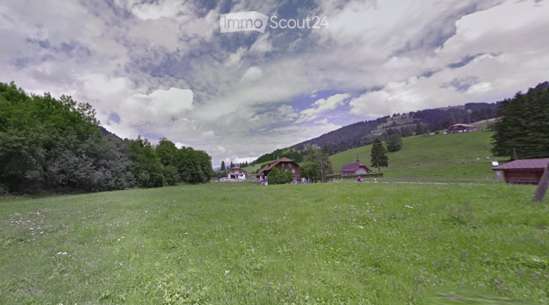A serene rural landscape with green fields, scattered houses, and trees under a partly cloudy sky.
