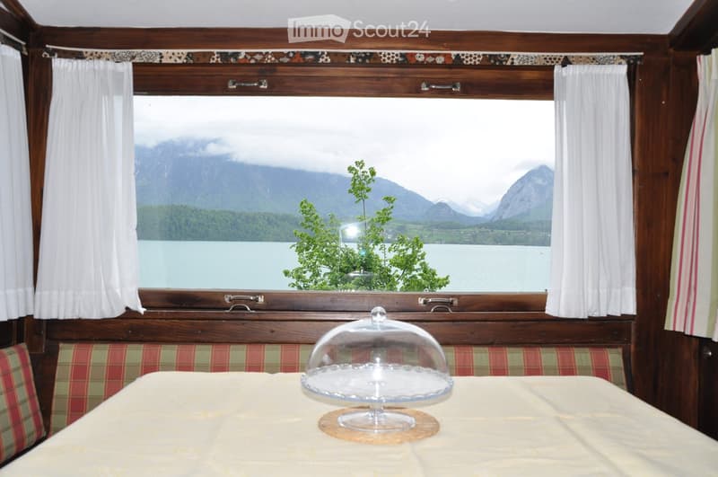 A cozy dining area with a large window showcasing a scenic mountain and lake view, featuring a table with a cake and plaid-patterned seating.