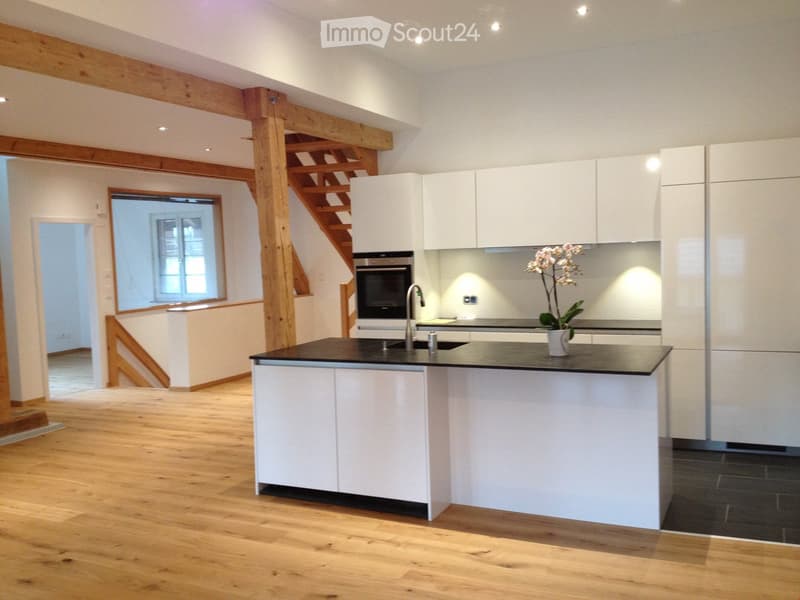 Modern kitchen with white cabinets, a central island, and a staircase leading to an upper level. Features include a sink, faucet, oven, and a decorative flower vase on the island.