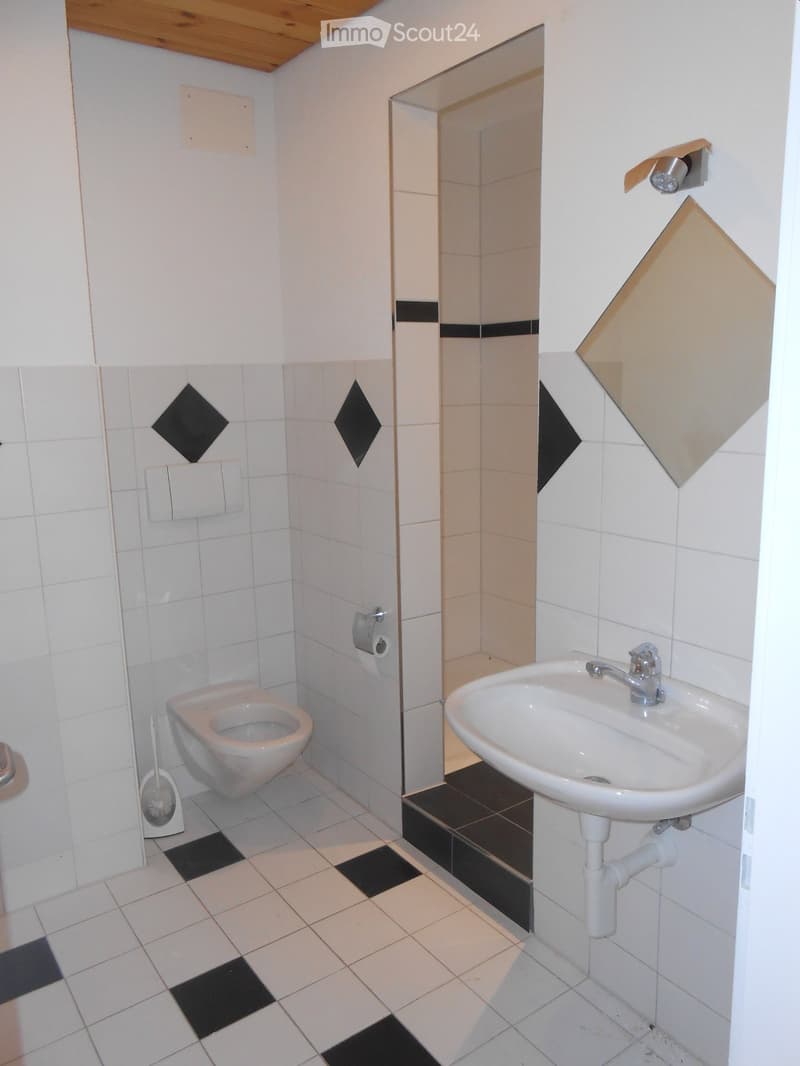 Small bathroom with white tiled walls and black diamond-shaped tiles, featuring a toilet, sink, and a glass shower enclosure.
