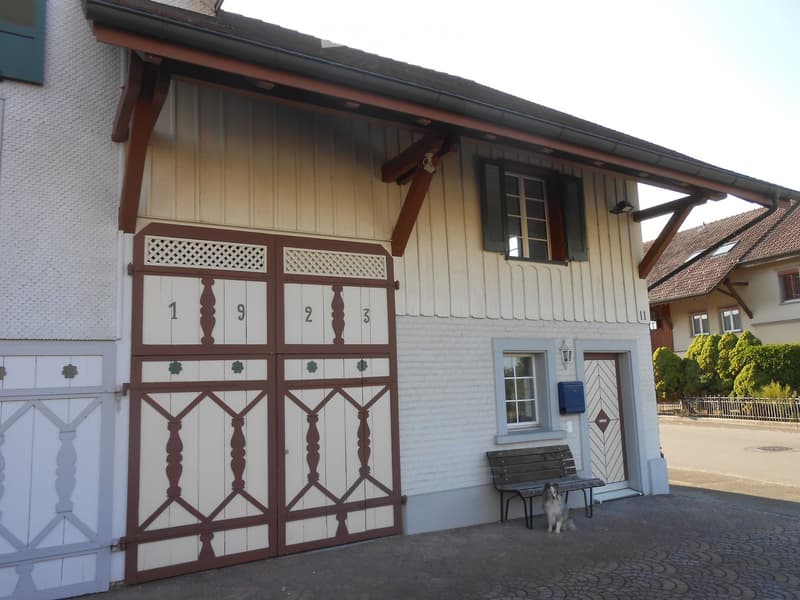 A two-story building with a large garage door featuring decorative numbers and patterns, a small bench, and a dog sitting nearby.
