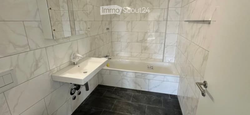 Modern bathroom with marble tiles, a white bathtub, a sink with a chrome faucet, and a large mirror above the sink.