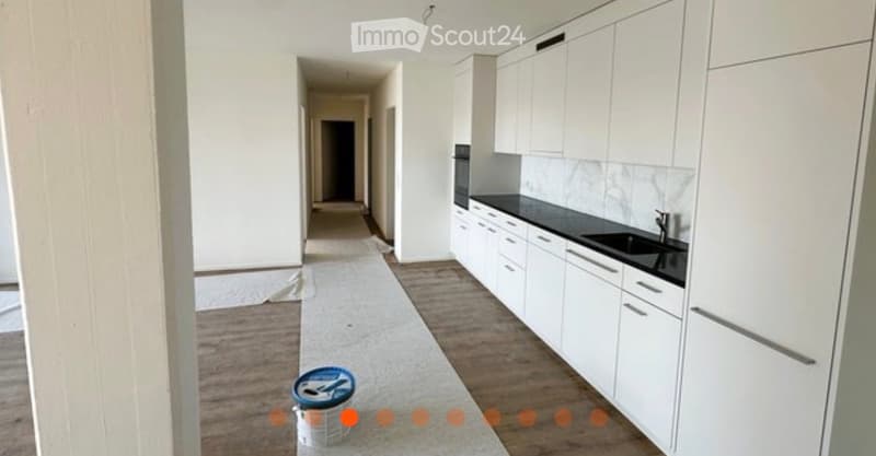 Modern kitchen with white cabinets, black countertops, and a sleek sink. The floor is wooden, and a hallway leads to another room.