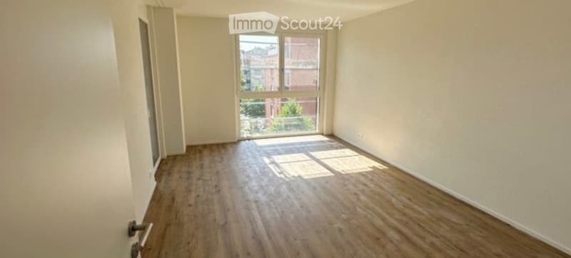 Empty room with wooden flooring and large window letting in natural light. No furniture or equipment present.