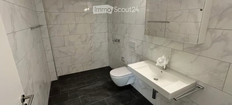 Modern bathroom with marble tiles, a white toilet, a white sink, a mirror, and a cabinet.