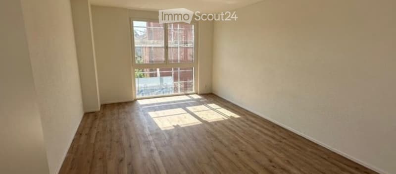 Empty room with wooden flooring and large window letting in natural light. No furniture or equipment present.