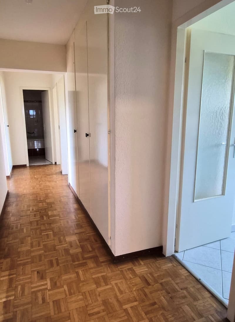 Empty hallway with wooden herringbone flooring, white walls, and multiple doors leading to other rooms.