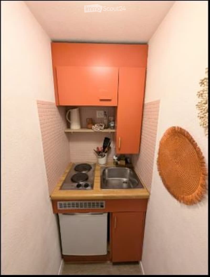 Compact kitchen with orange cabinets, a stove, sink, dishwasher, and a wicker basket on the wall.