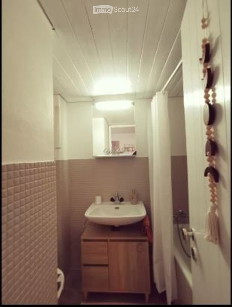 Small bathroom with a white sink, wooden cabinet, mirror, and tiled walls.