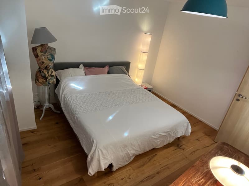 Cozy bedroom with a double bed, white bedding, wooden floor, and modern lighting.