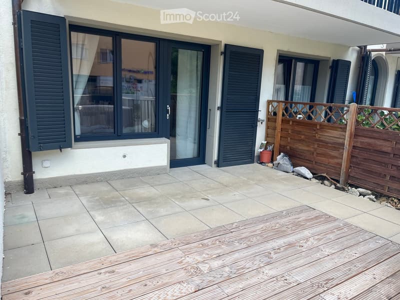 Balcony area with tiled floor, wooden deck, wooden fence, and large windows with shutters leading to the interior.