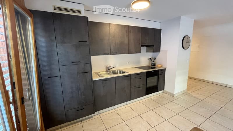Modern kitchen with dark grey cabinets, a sink, an oven, and a clock on the wall.