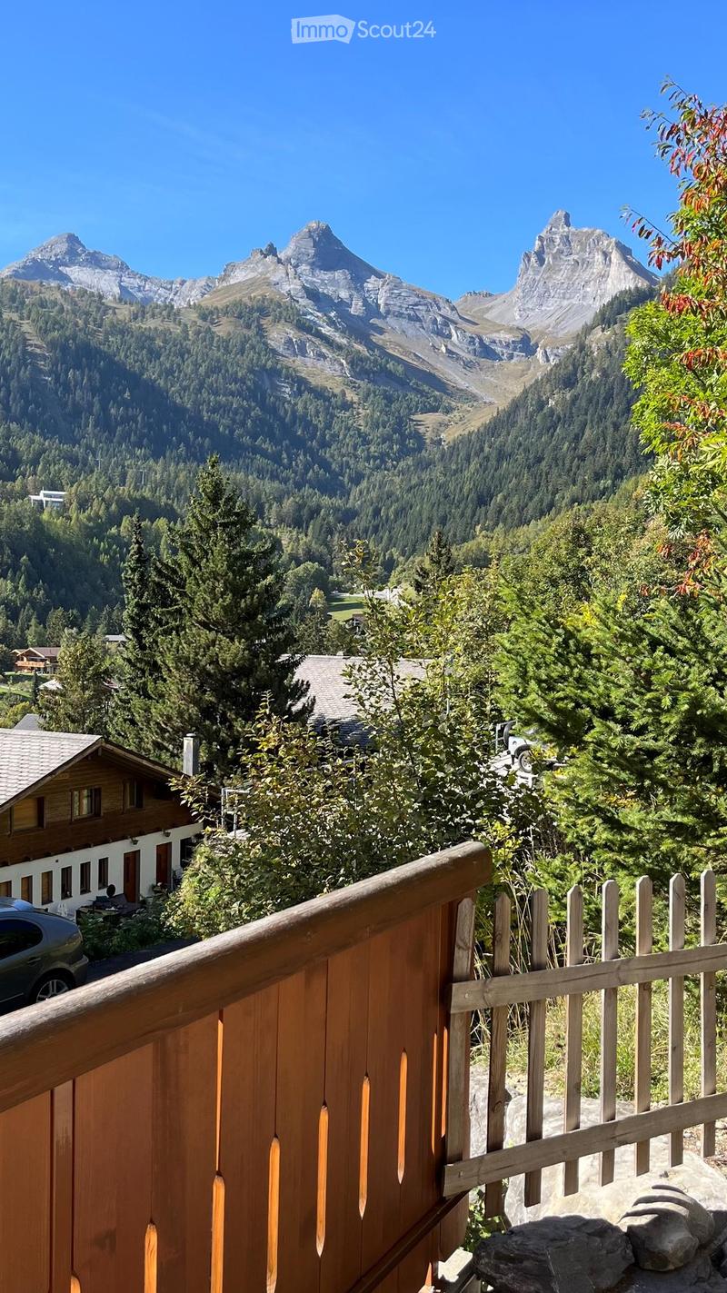 Balcony overlooking a lush green valley with dense forests and distant snow-capped mountains.