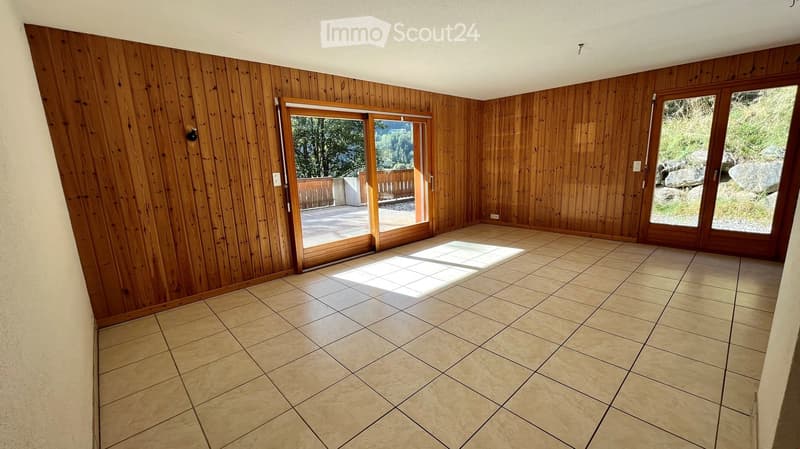 Empty room with wooden walls and tiled floor, featuring large sliding glass doors leading to an outdoor area.
