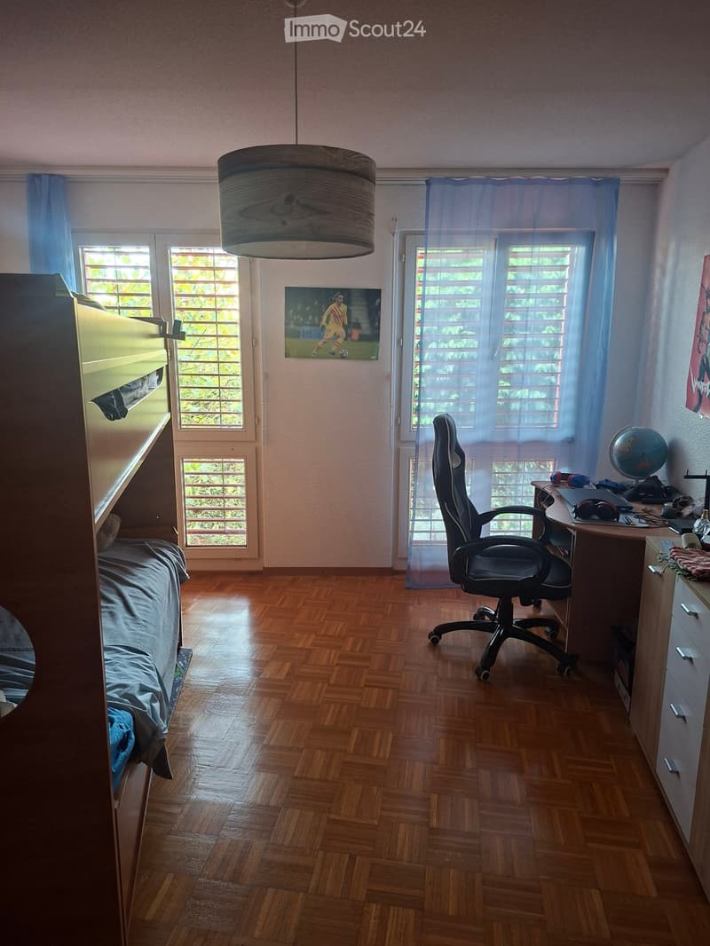 Bright bedroom with wooden flooring, bunk bed, desk with chair, globe, and picture on wall.