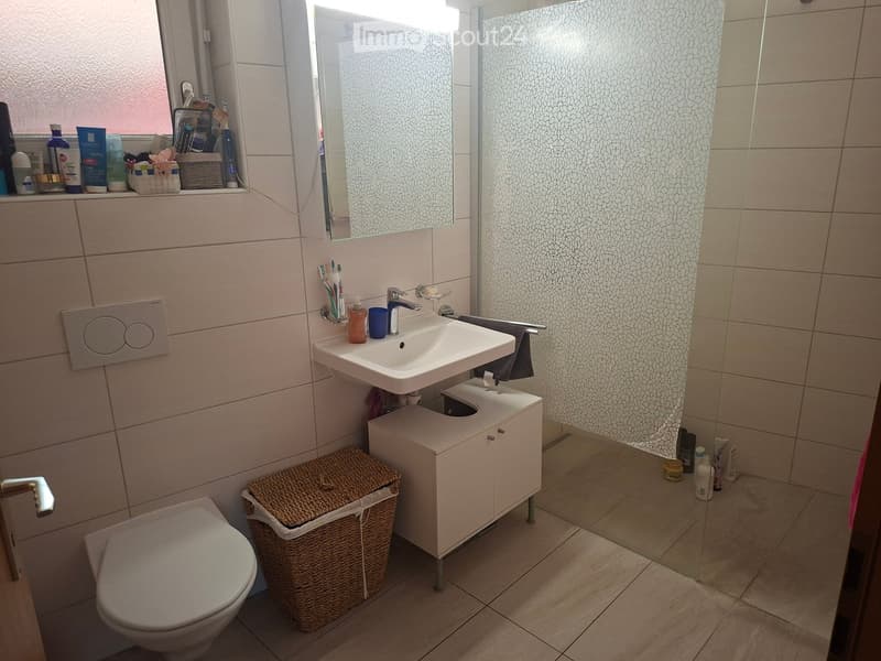 Modern bathroom with a white sink, toilet, mirror, and cabinet. Includes a wicker basket and various toiletries on the windowsill and floor.