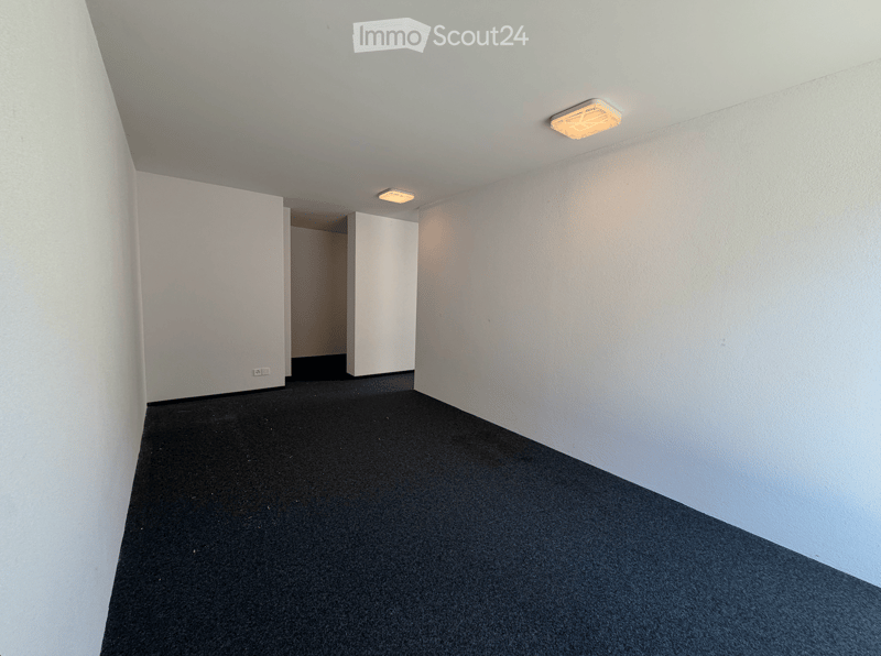 Empty room with white walls, black carpeted floor, and recessed lighting. No furniture or equipment present.