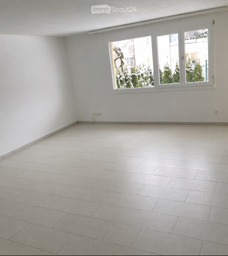 Empty room with white walls, tiled floor, and large window with white frame. No furniture or equipment present.