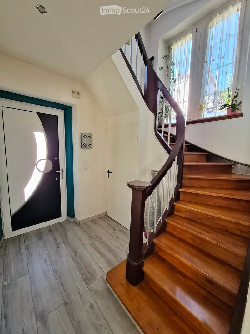 Hallway with wooden staircase, grey tiled floor, white walls, and a door leading outside.