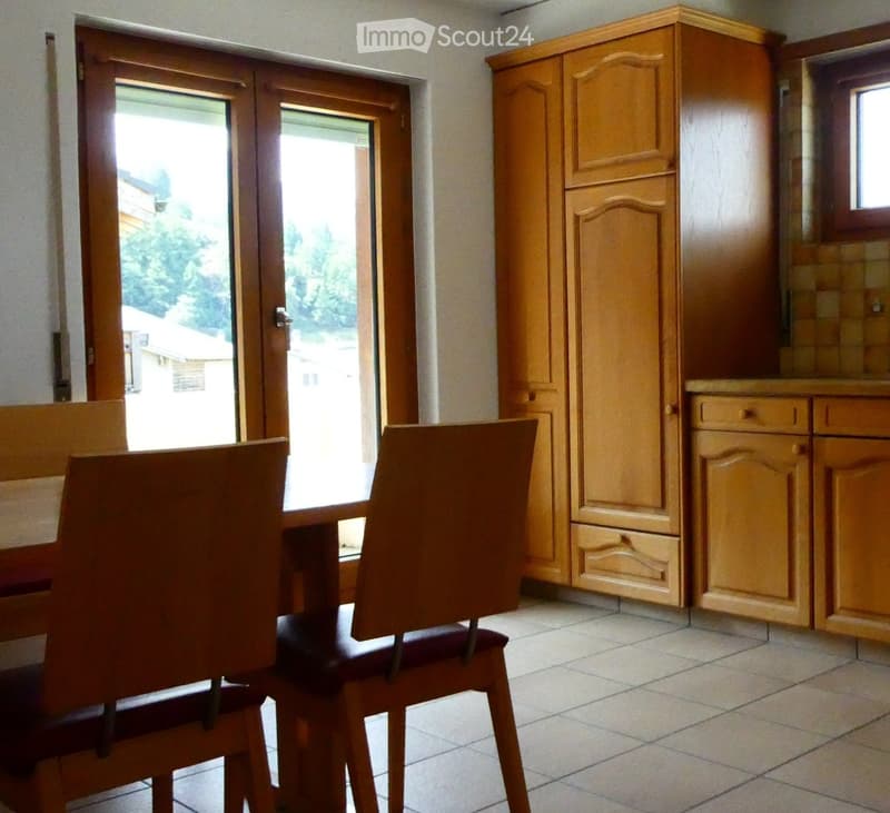 Dining area with wooden chairs, a table, and wooden cabinets, with a sliding glass door leading outside.