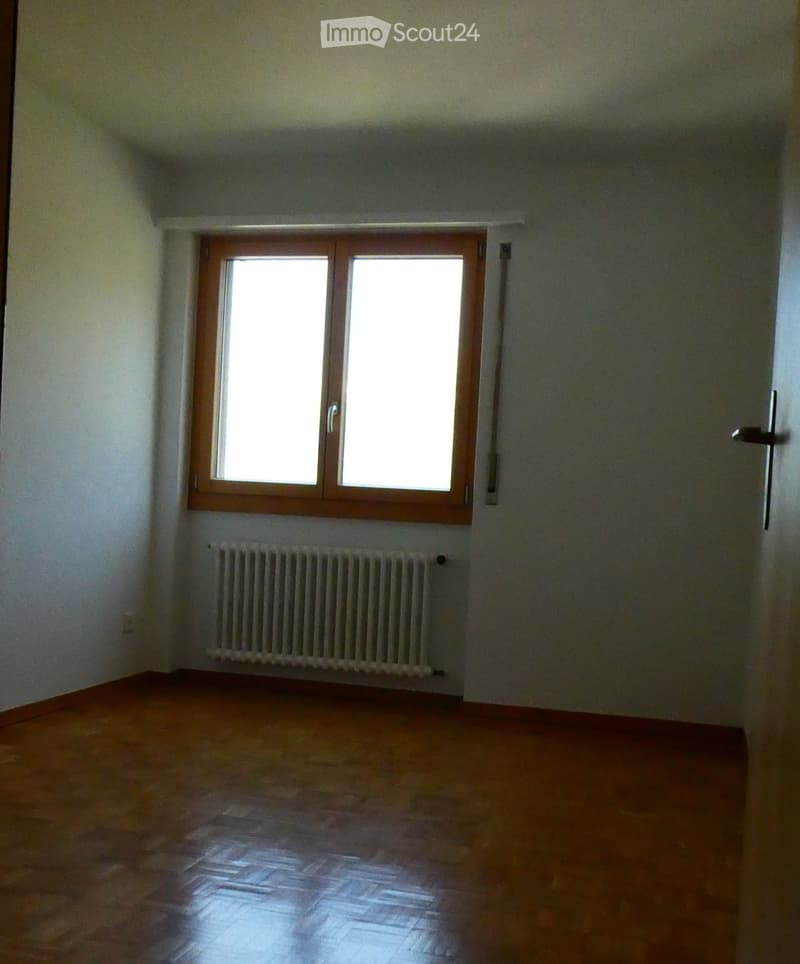 Empty room with wooden flooring, white walls, a window with wooden frame, and a radiator below the window.