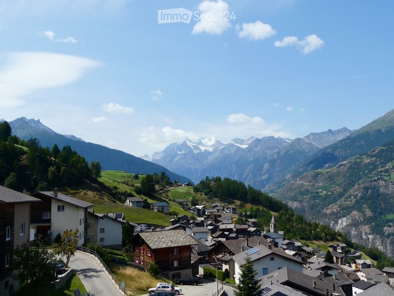 A picturesque village nestled in a valley with snow-capped mountains in the background, featuring traditional houses and a winding road.
