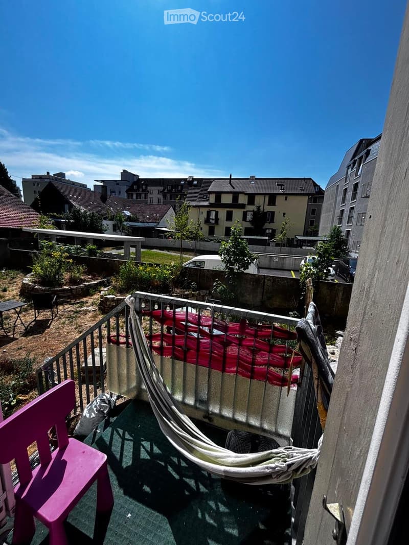 Balcony with a pink chair, a hammock, and a view of the city with buildings and greenery.