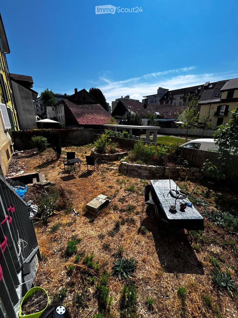 Small garden area with a table and chairs, surrounded by low stone walls and sparse vegetation.
