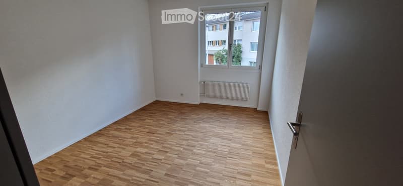 Empty room with wooden flooring, white walls, and a window with a radiator below it.