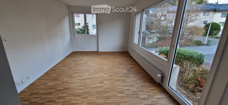 Empty room with wooden flooring, white walls, large windows, and a radiator. No furniture or equipment present.