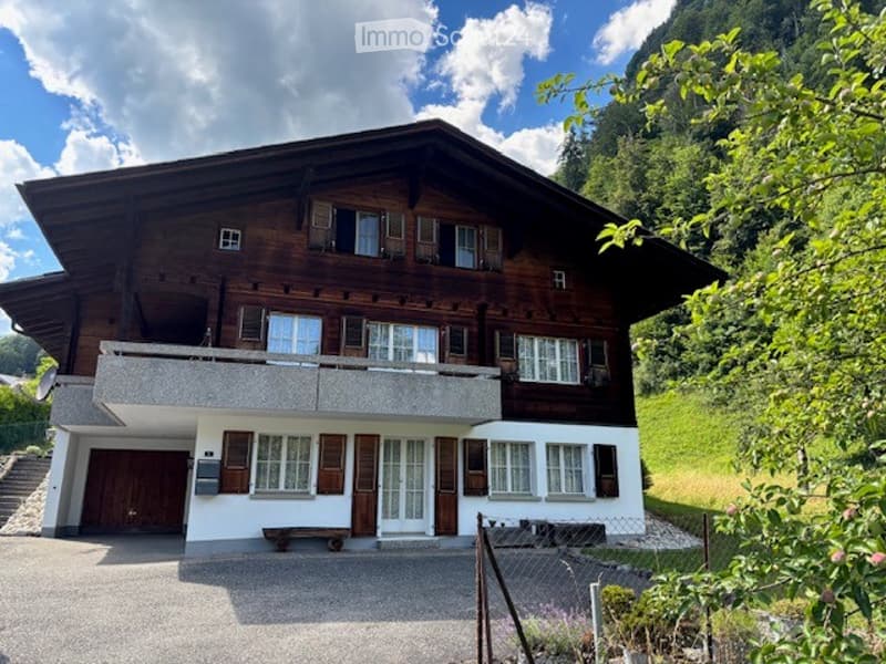 Traditional wooden chalet with multiple windows, garage, and scenic mountain view.