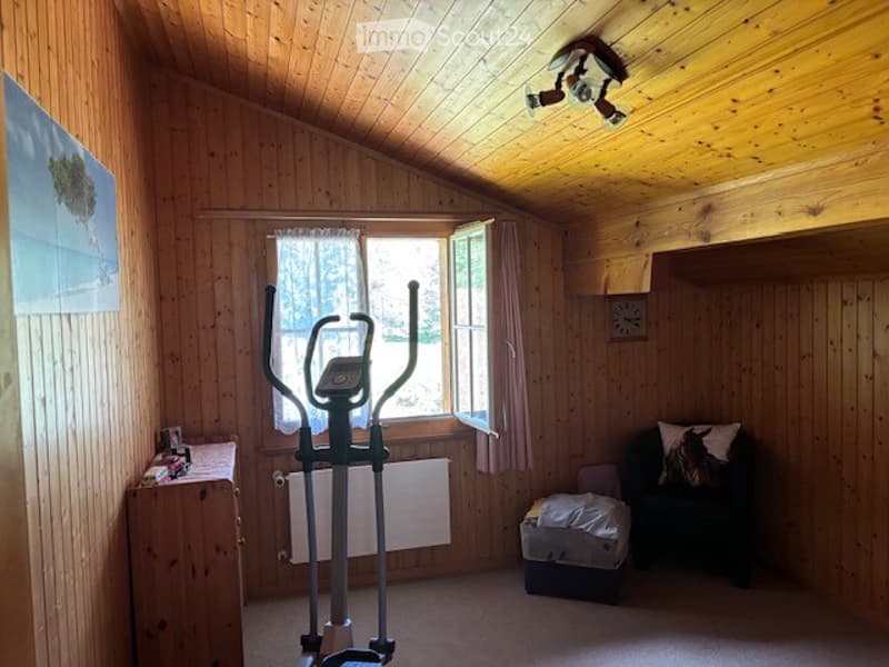 Wooden-paneled room with exercise bike, sofa, small table, and window with curtains.