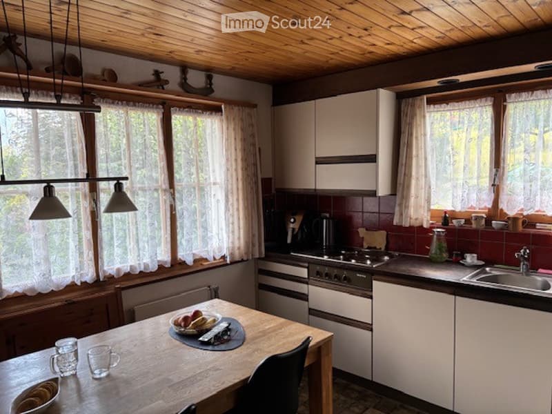 Bright kitchen with wooden ceiling, large windows, white cabinets, and a dining area with a wooden table and chairs.