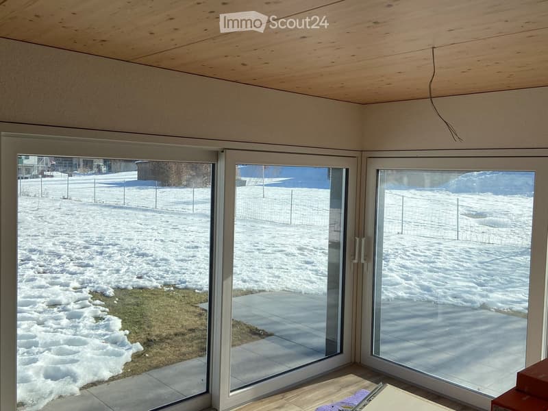 An unfurnished room with large glass sliding doors leading to a snowy outdoor area. The room features a wooden ceiling and tiled floor.