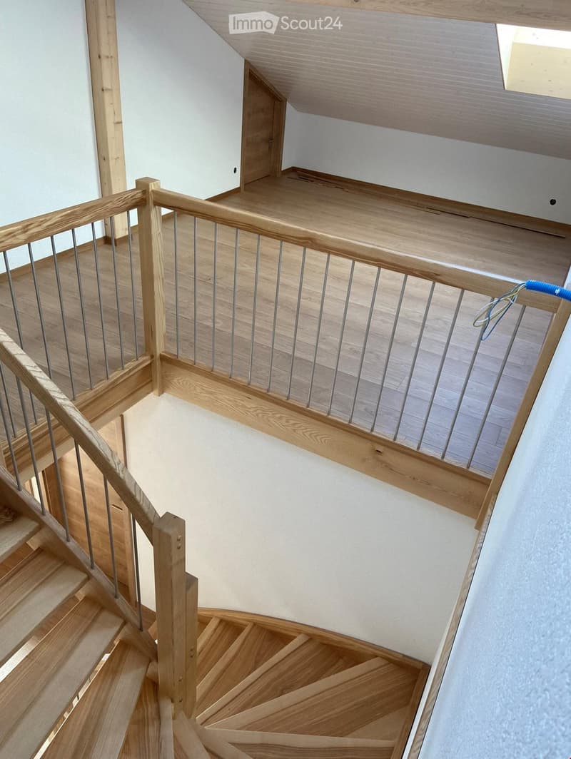Spiral staircase with wooden steps and handrail, metal balusters, white walls, and a skylight at the top.