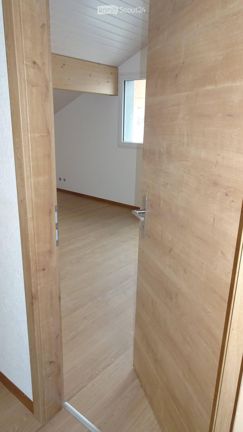 Empty hallway with light wooden flooring and white walls, featuring a partially open wooden door and a small window at the end.