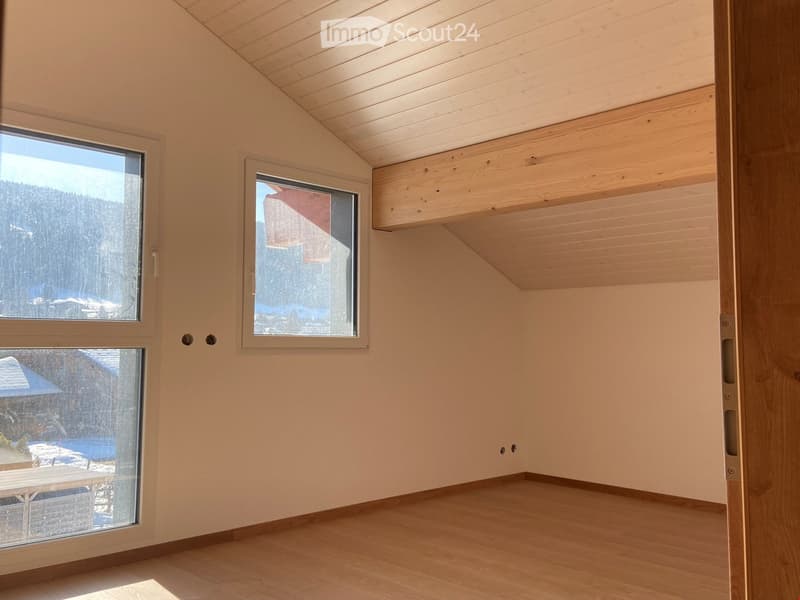 Empty room with wooden flooring, light-colored walls, and large windows offering a view of a snowy landscape.