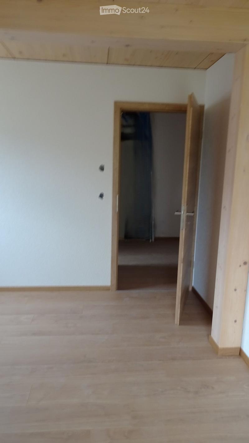Empty hallway with wooden flooring and white walls, featuring an open doorway leading to another room.