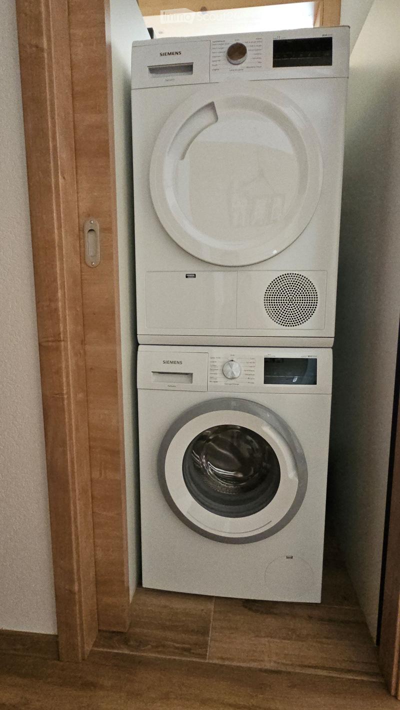 A compact bathroom with a stacked Siemens washing machine and dryer unit, featuring a control panel and a drum paddle.
