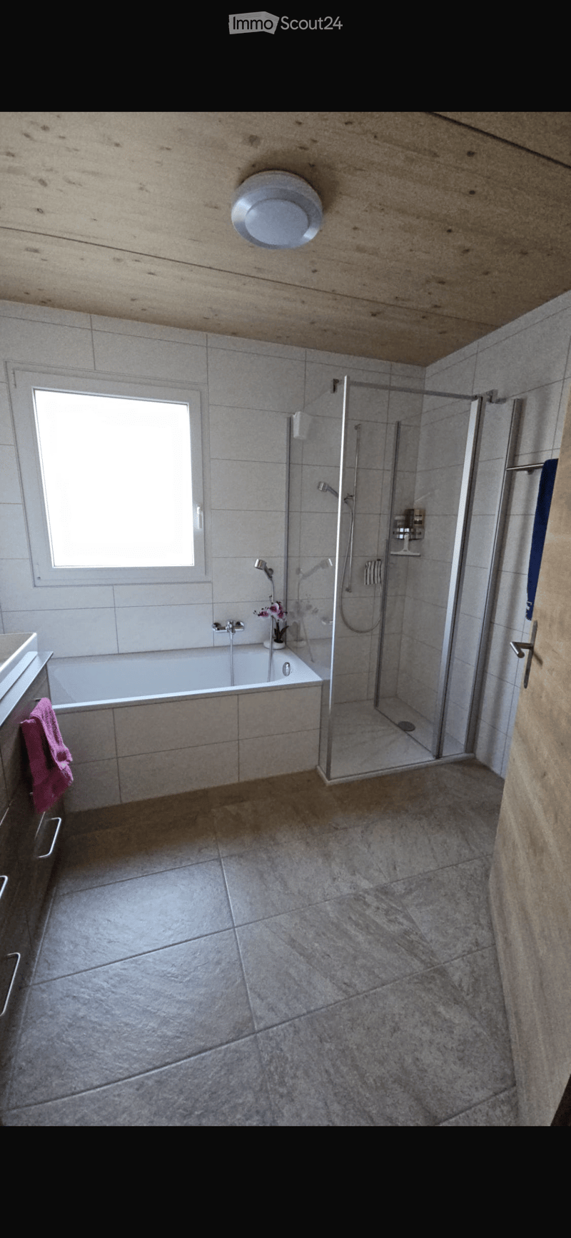 Modern bathroom with a bathtub, glass-enclosed shower, tiled walls and floor, and a window providing natural light.