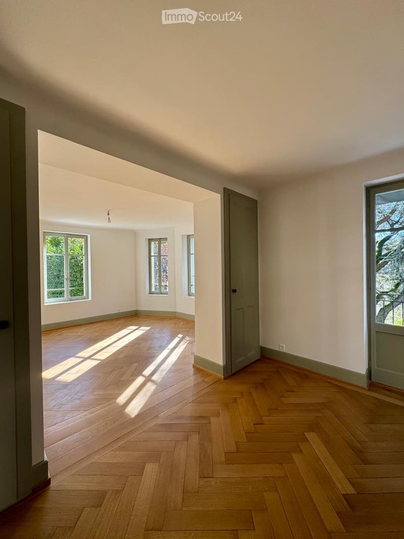 Empty room with parquet flooring, white walls, three windows with natural light, doors