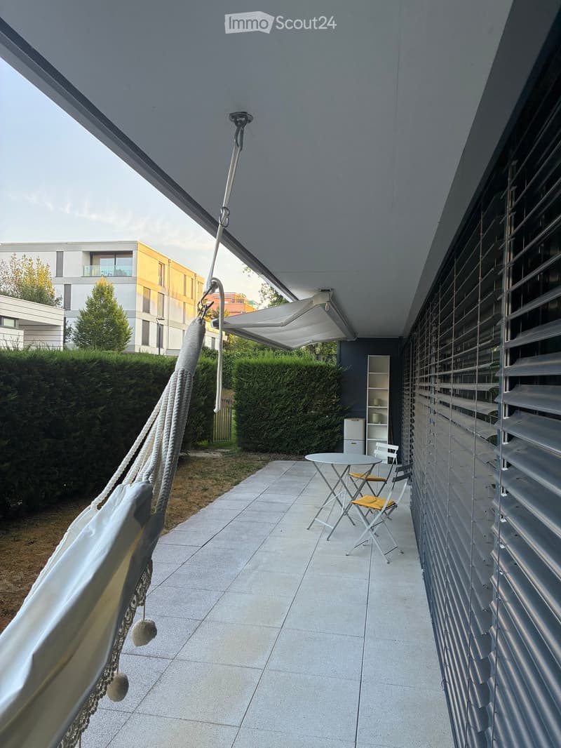 Balcony with tiled floor, outdoor table and chairs, hammock, and retractable awning.