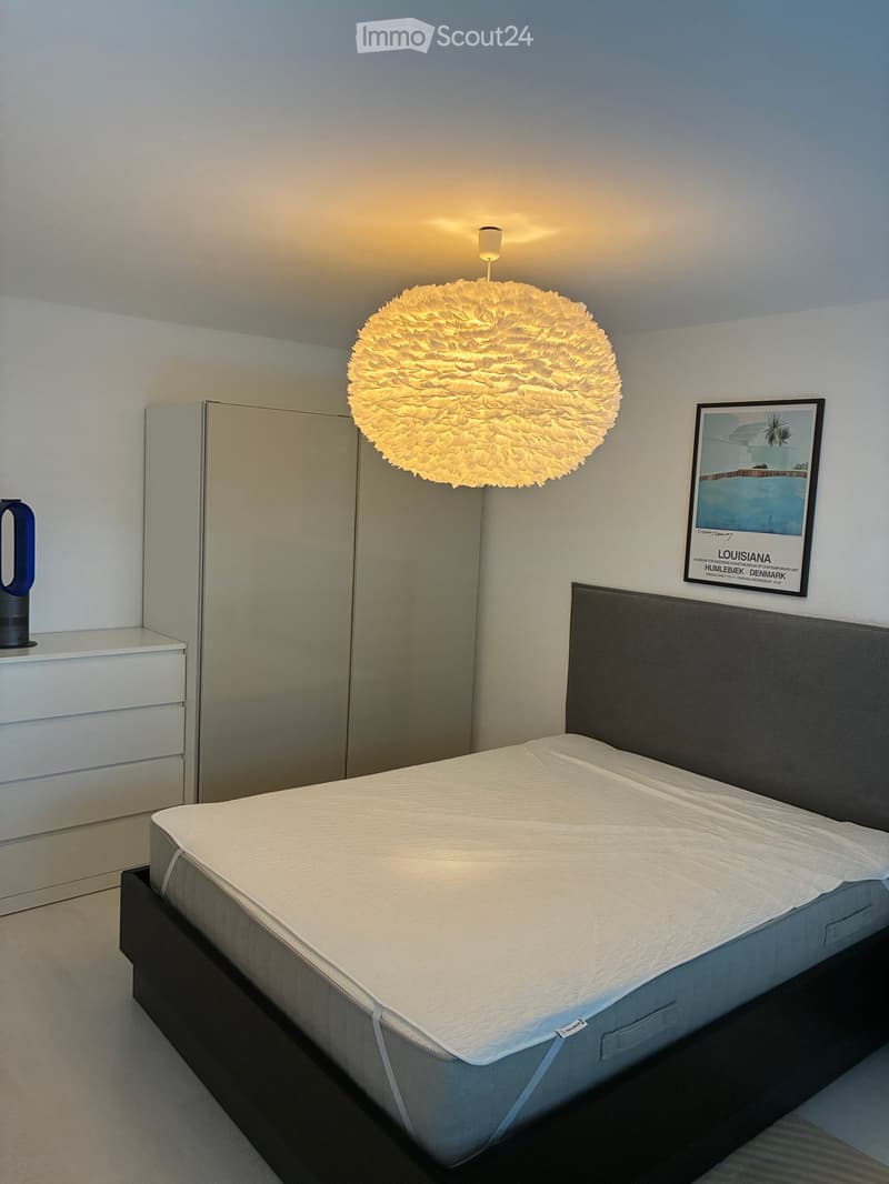 Modern bedroom with a large bed, nightstand, decorative lamp, and artwork on the wall.