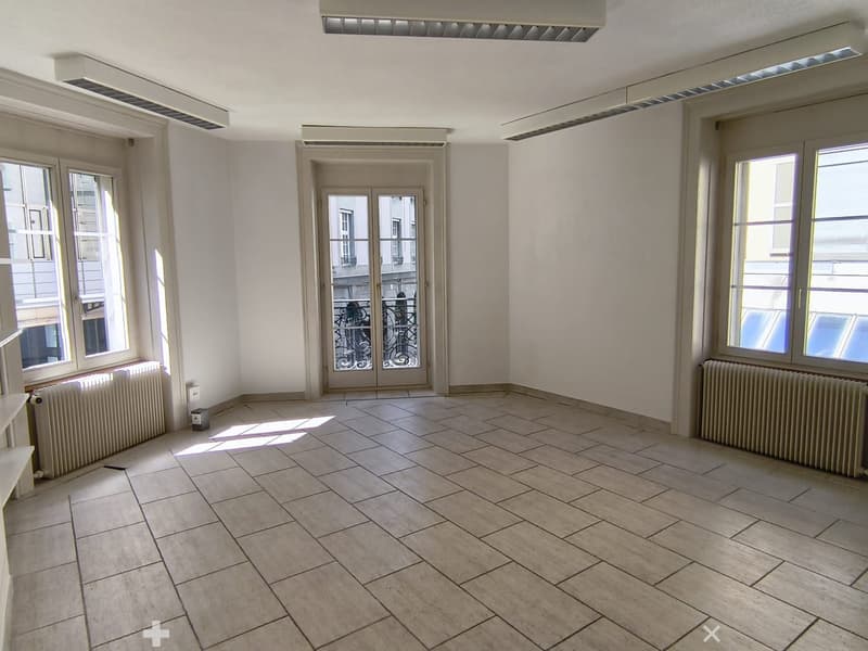 Empty room with tiled floor, white walls, large windows, and a door leading to a balcony.