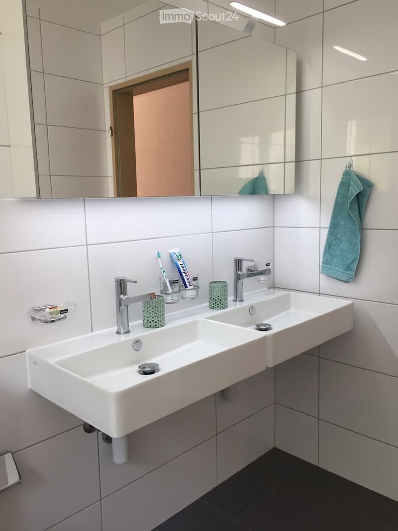 Modern bathroom with a double sink, chrome faucets, toothbrush holders, and a towel hanging on the wall.